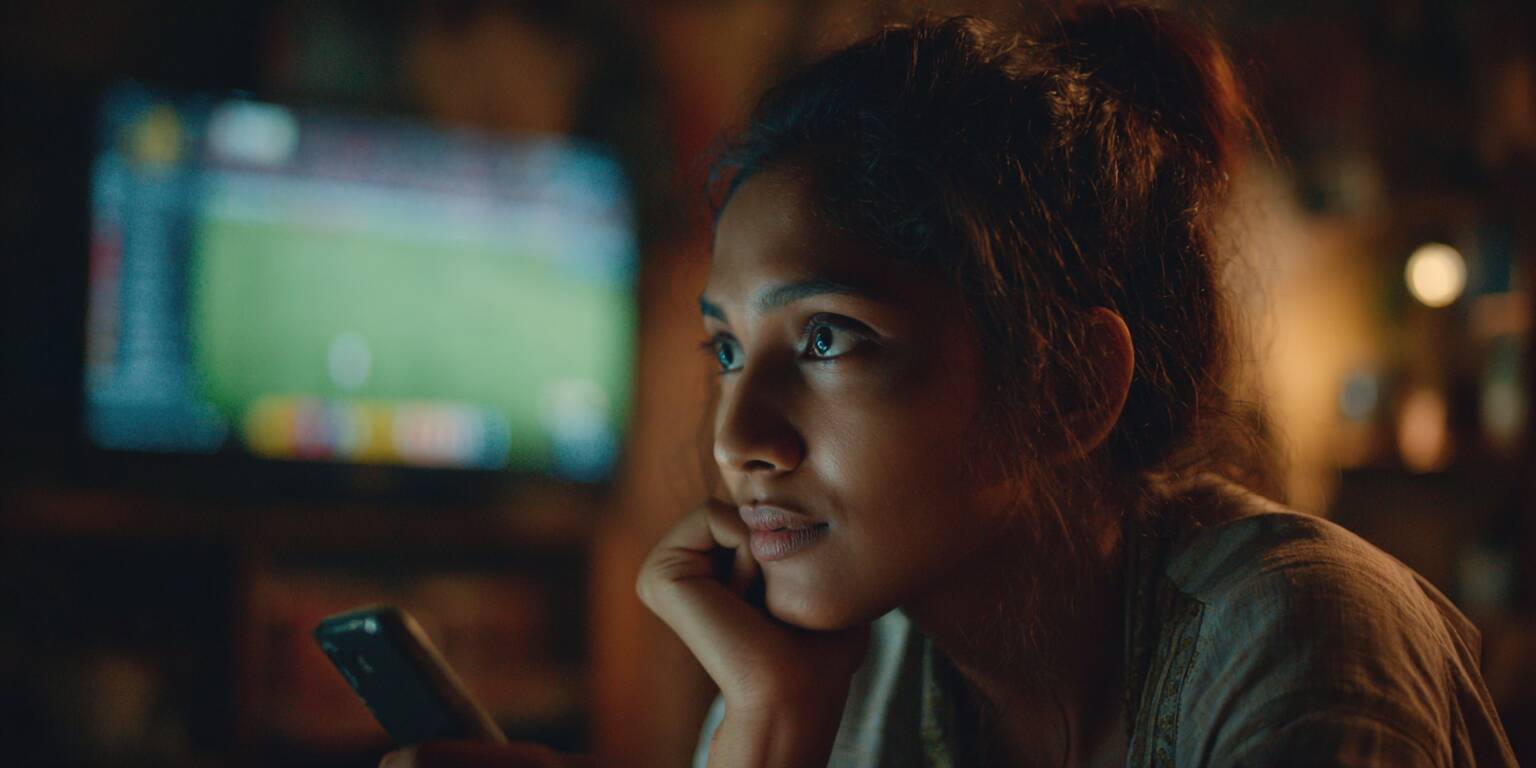 A beautiful young woman from Bangladesh, looking excited and focused while watching a live cricket match and placing a bet on her smartphone.